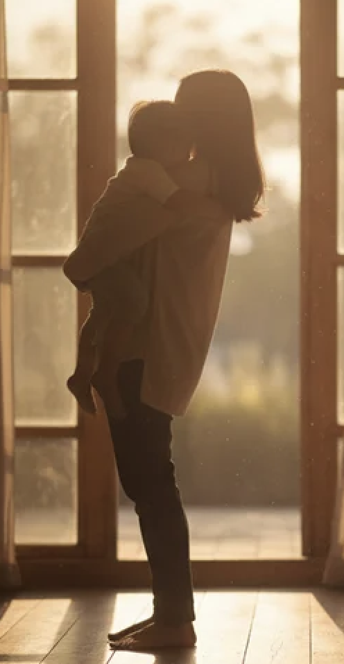 Woman holding child by window with golden light